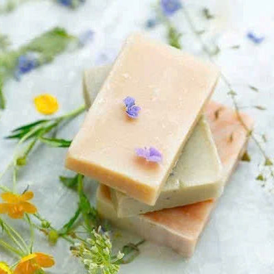 Three bars of soap stacked on a white surface with flowers and greenery.